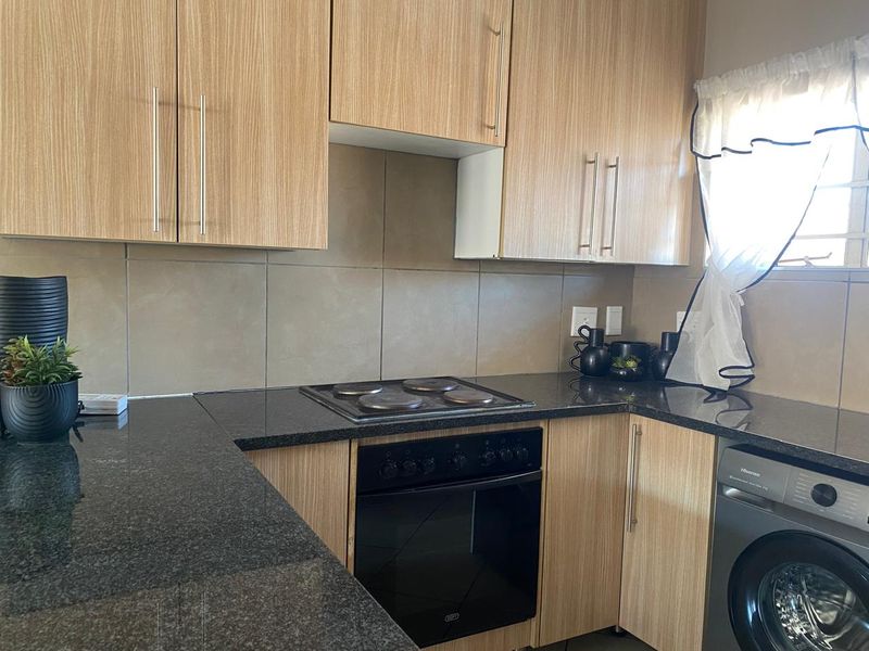 A functional kitchen featuring light wood-finish cabinetry, dark granite countertops, a built-in oven with electric hob, and a tiled backsplash.