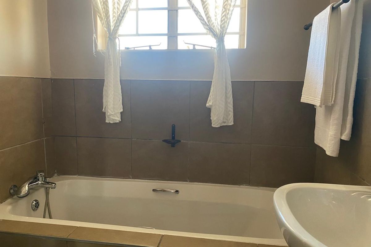 A functional bathroom featuring a built-in bathtub with wall-mounted fixtures, tiled splashback, and a pedestal basin.