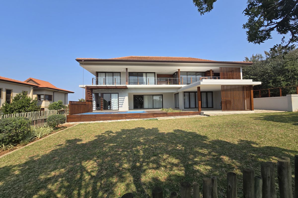 A modern two-story residence featuring a rear swimming pool, timber decking, expansive balconies, and large sliding glass doors overlooking a landscaped garden.