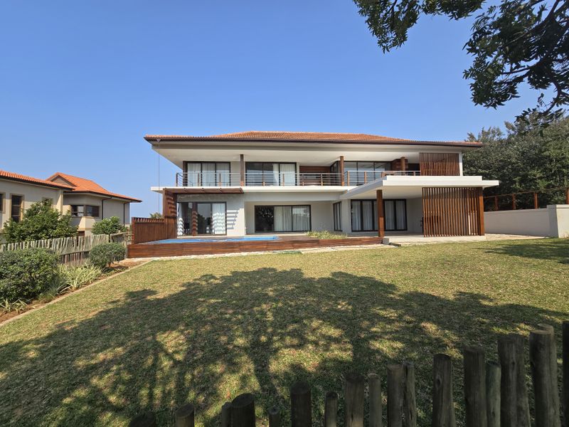 A modern two-story residence featuring a rear swimming pool, timber decking, expansive balconies, and large sliding glass doors overlooking a landscaped garden.