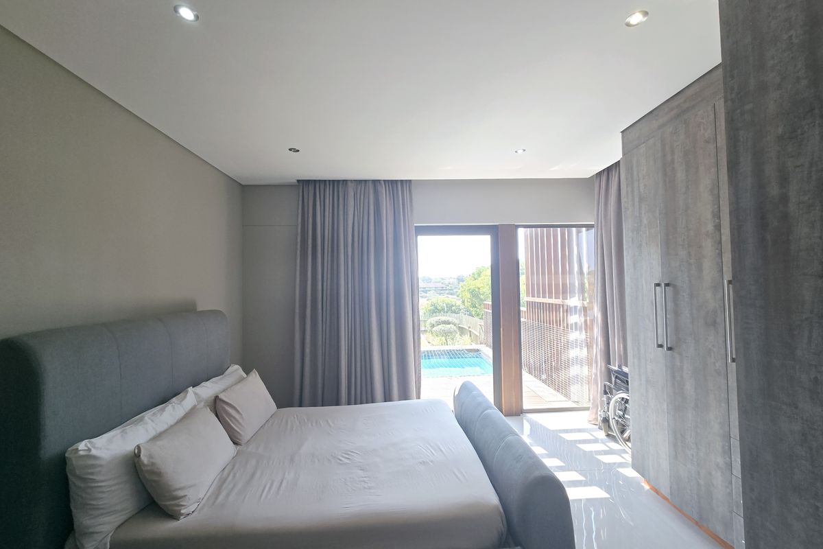 Modern bedroom featuring built-in cupboards, recessed lighting, and direct access to a private patio and pool area through sliding glass doors.