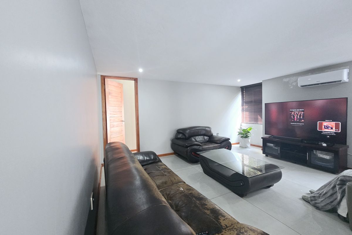 A well-maintained living room featuring neutral tiled flooring, recessed downlighting, and a wall-mounted air conditioning unit.