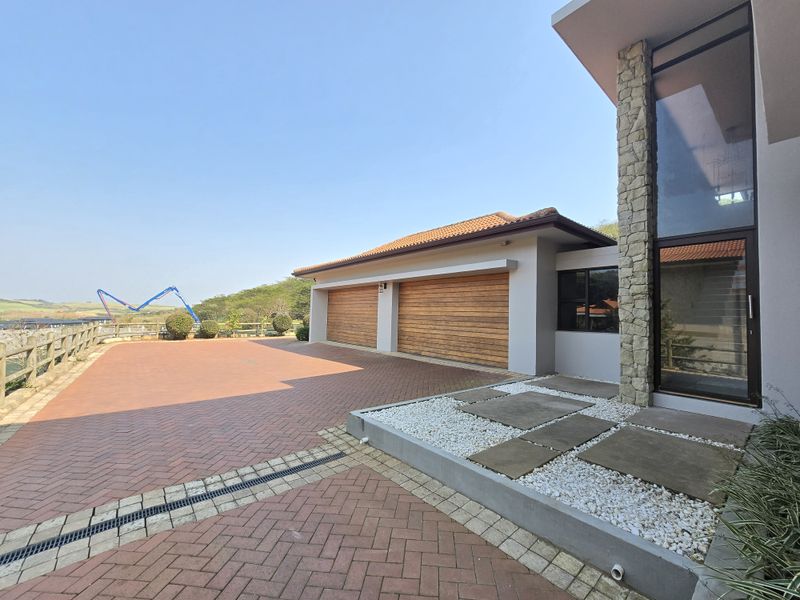 A modern front exterior featuring a double garage with timber doors, stone cladding accents, and a neatly paved driveway with integrated drainage.
