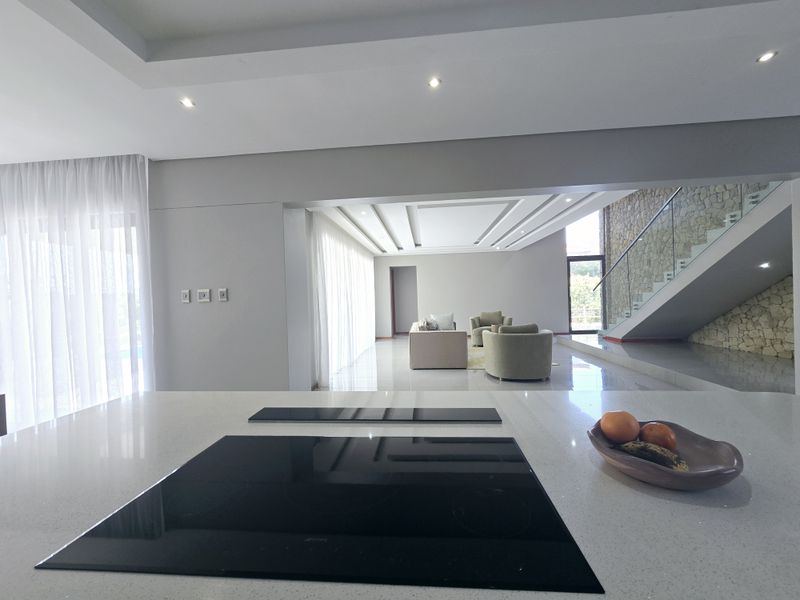 Spacious open-plan living area featuring a modern kitchen island with induction hob, stone feature wall, and elegant staircase with glass balustrade.