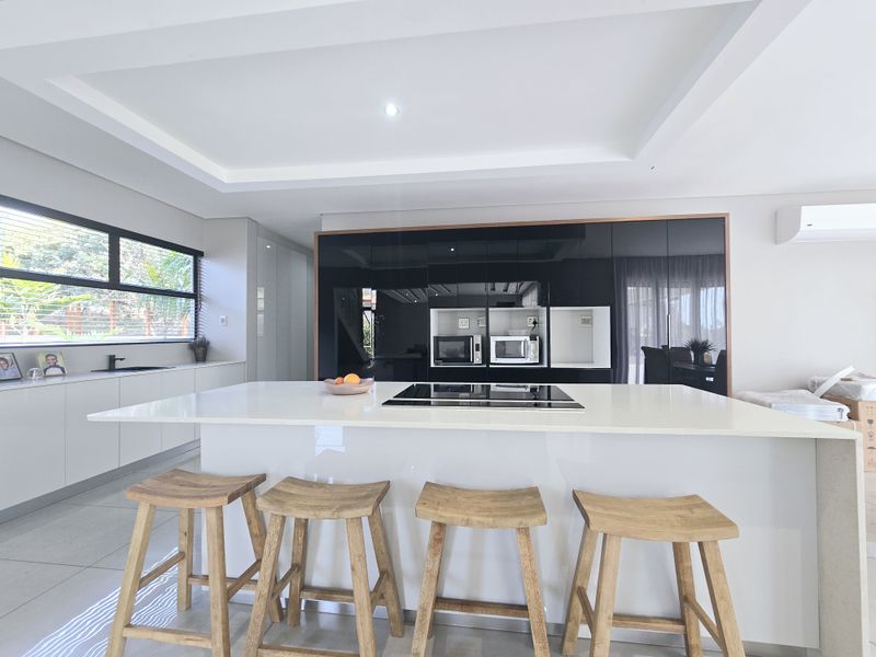 Modern kitchen featuring a large central island with a built-in hob, sleek high-gloss cabinetry, and integrated appliances under a stylish recessed ceiling.