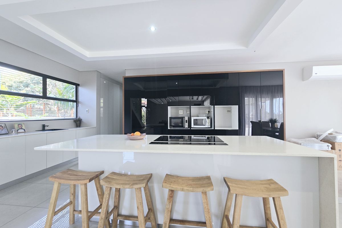 Modern kitchen featuring a large central island with a built-in hob, sleek high-gloss cabinetry, and integrated appliances under a stylish recessed ceiling.