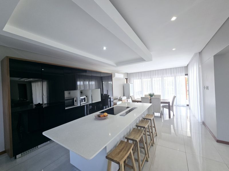 Modern open-plan living area featuring a sleek kitchen island with integrated cooktop, high-gloss cabinetry, and polished tiled flooring throughout.