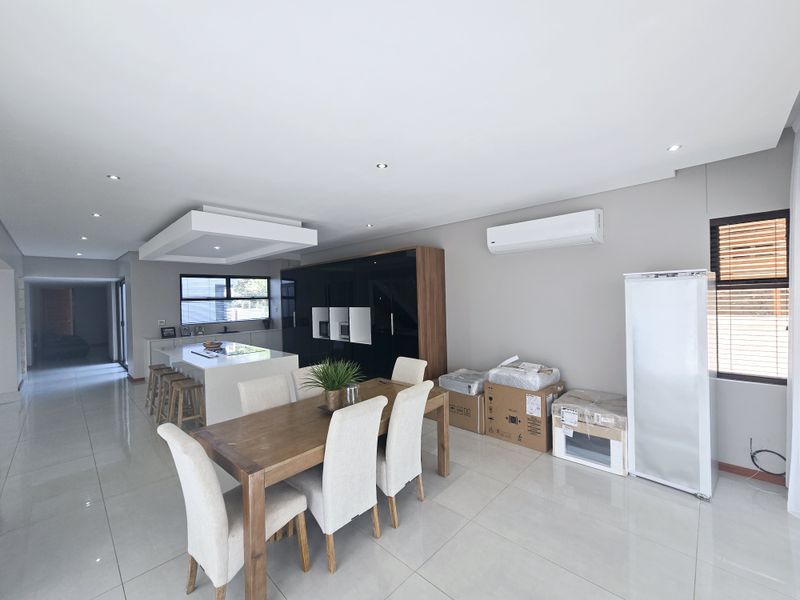 Spacious open-plan living and dining area featuring a modern kitchen island, sleek built-in cabinetry, recessed lighting, and polished tiled flooring throughout.