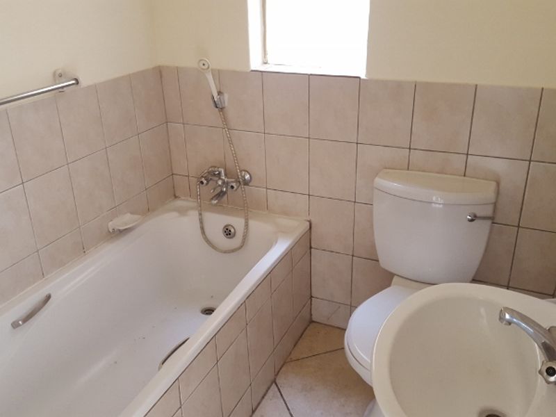A functional bathroom featuring a bathtub with handheld shower attachment, a standard toilet, and a pedestal basin with tiled finishes throughout.