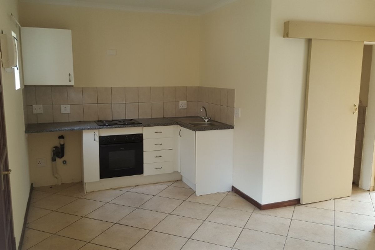 A compact kitchen featuring built-in cabinetry, a gas hob, an oven, and tiled flooring, currently vacant and ready for updates.
