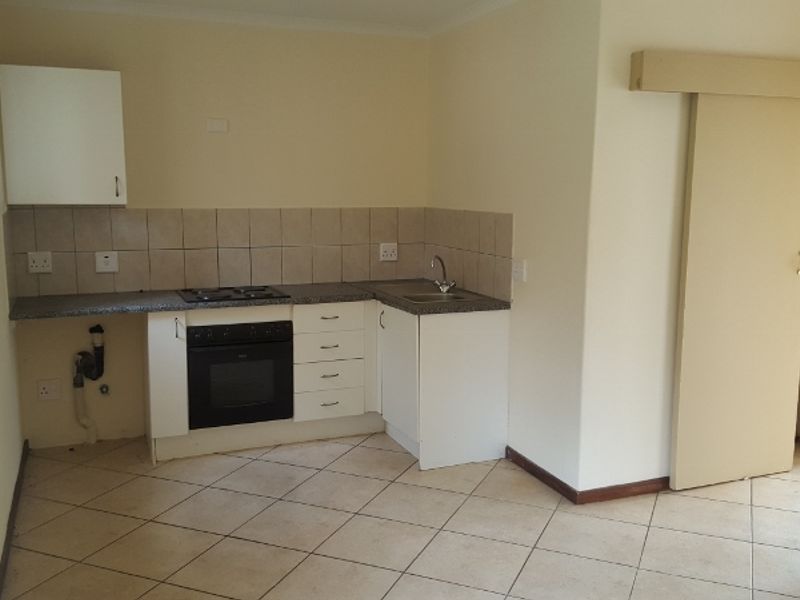 A compact kitchen featuring built-in cabinetry, a gas hob, an oven, and tiled flooring, currently vacant and ready for updates.