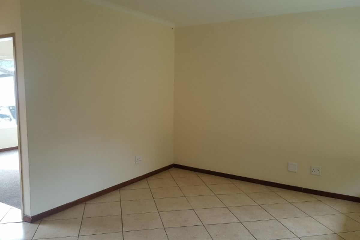 An empty living area featuring neutral walls, ceramic floor tiles, and a doorway leading to an adjacent space.