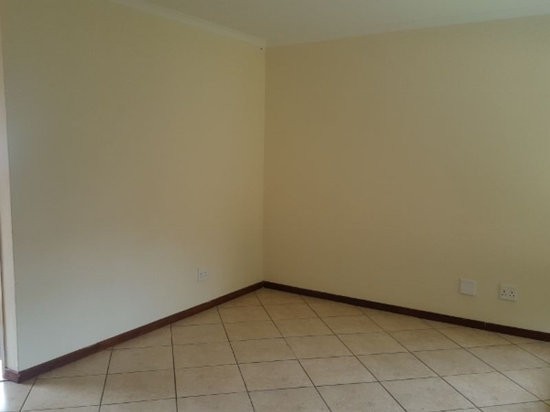 An empty living area featuring neutral walls, ceramic floor tiles, and a doorway leading to an adjacent space.