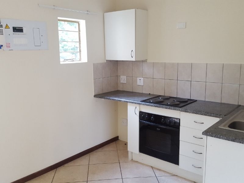 A compact, functional kitchen featuring built-in cabinetry, an integrated oven and hob, tiled backsplash, and a stainless steel sink.