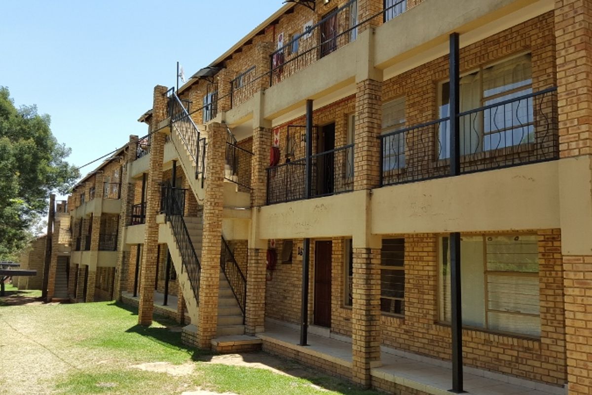 Exterior view of a multi-story apartment building featuring face brick construction, external staircases, and metal balcony railings.