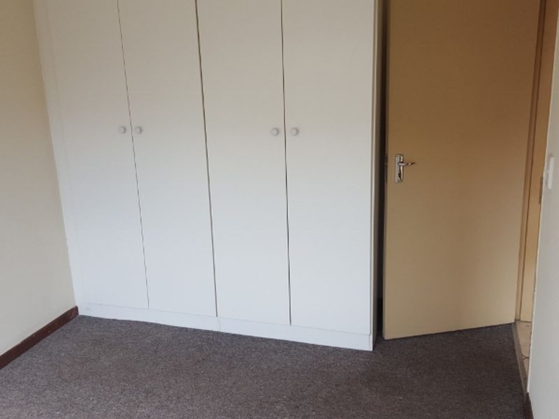 A simple, empty bedroom featuring neutral walls, carpeted flooring, and built-in white cupboards.