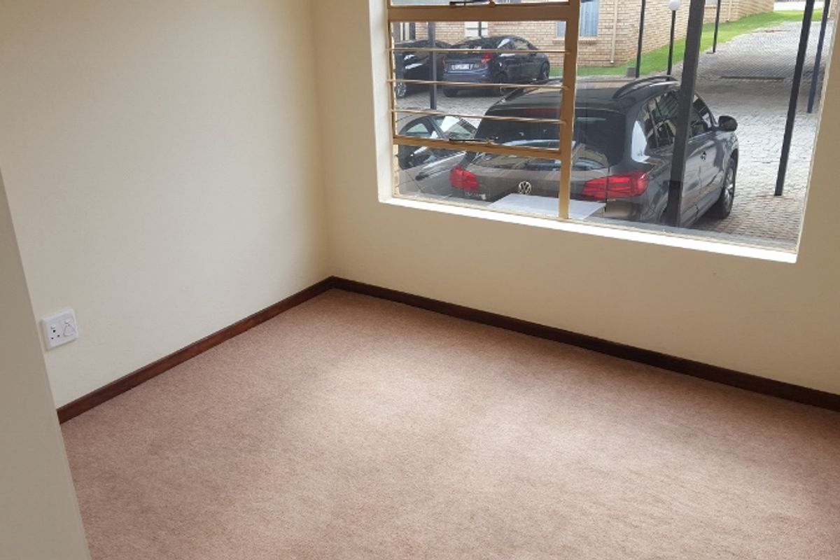 An empty bedroom featuring carpeted flooring and a window with security burglar bars, offering a view of the parking area.