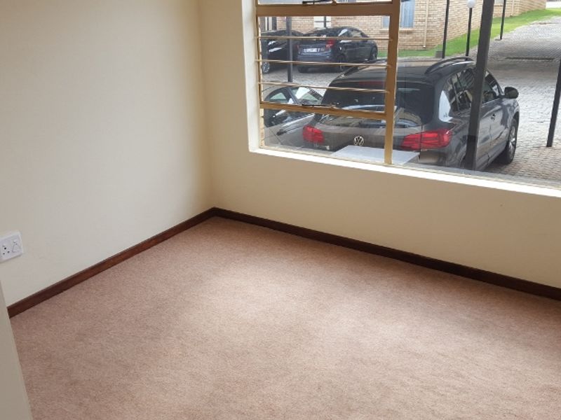 An empty bedroom featuring carpeted flooring and a window with security burglar bars, offering a view of the parking area.