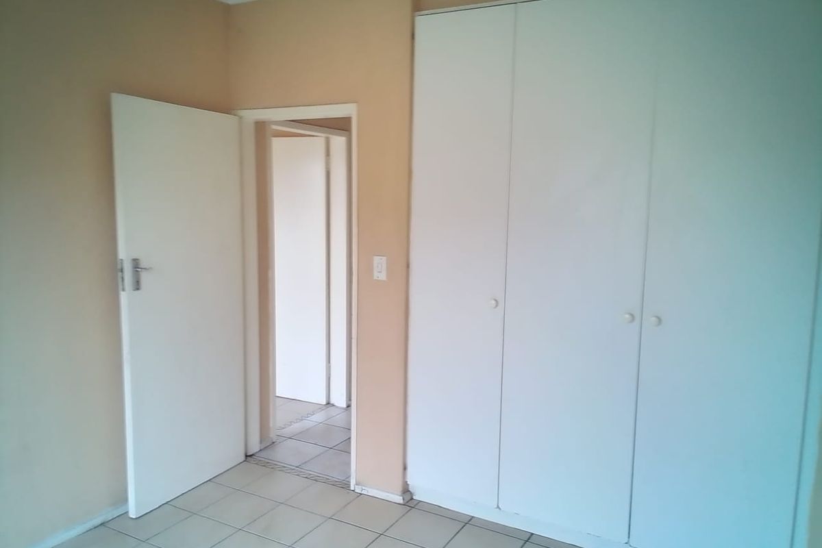 A vacant bedroom featuring neutral wall paint, tiled flooring, and white built-in cupboards, offering a clean canvas for personalization.