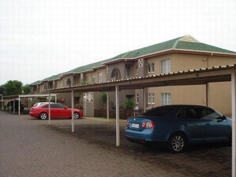 Exterior view of an apartment complex featuring covered parking bays and a paved driveway area.