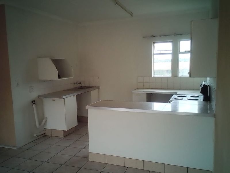 An empty, dated kitchen featuring tiled flooring, built-in cabinetry, a breakfast bar, and an electric hob, offering significant potential for renovation.