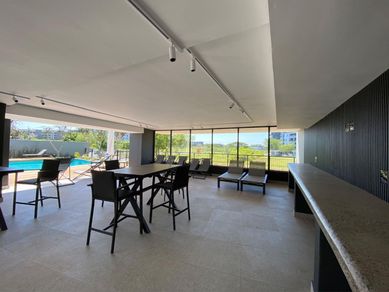 Spacious covered patio area featuring modern tiled flooring, track lighting, and a built-in bar counter, overlooking the swimming pool and landscaped grounds.