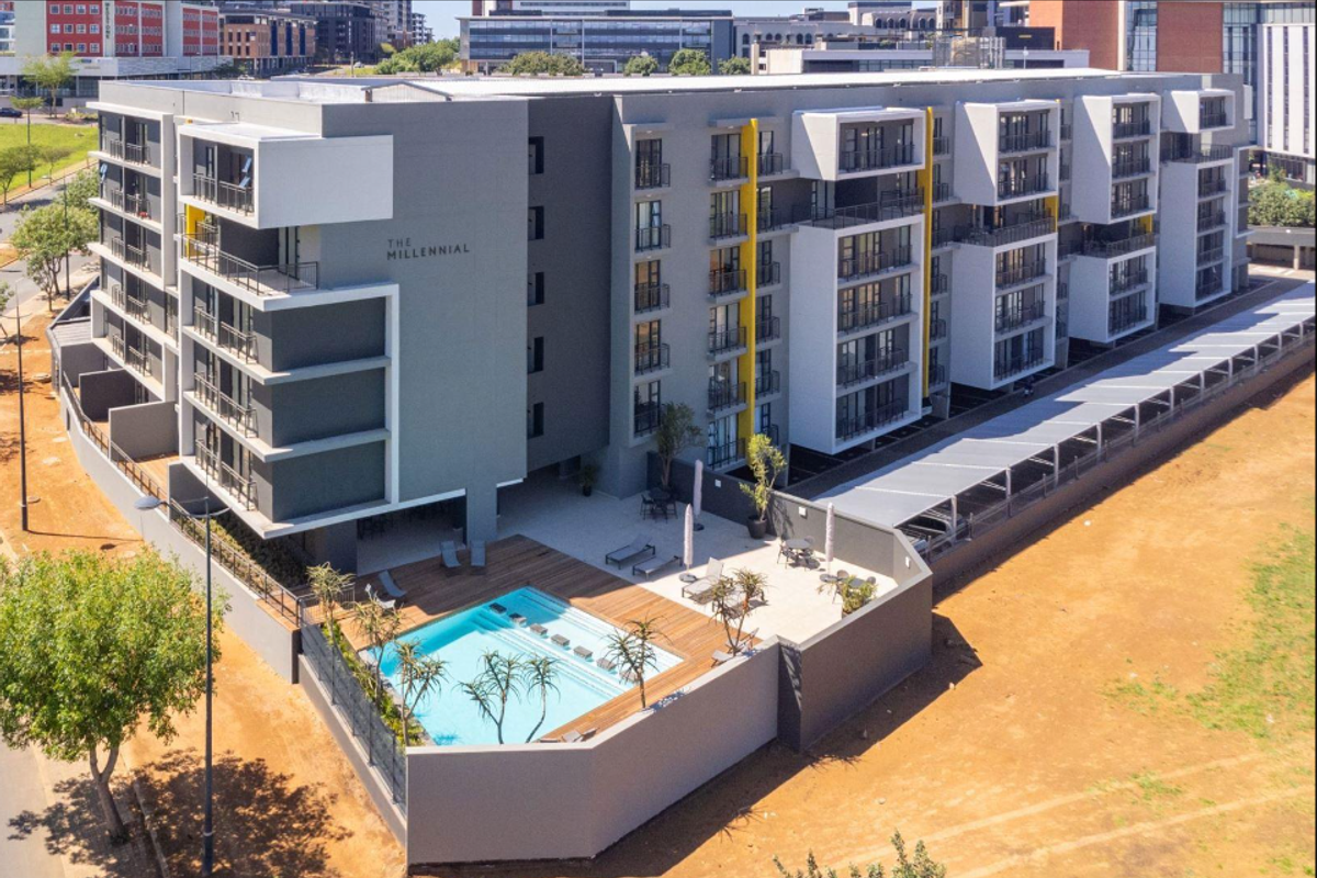 Aerial view of The Millennial apartment complex featuring a modern swimming pool, wooden decking, and covered parking facilities within a secure perimeter.