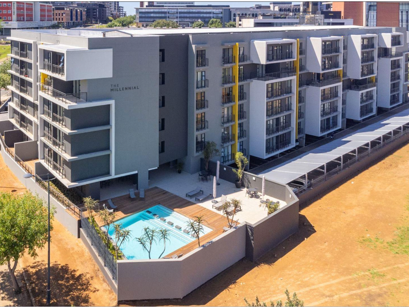 Aerial view of The Millennial apartment complex featuring a modern swimming pool, wooden decking, and covered parking facilities within a secure perimeter.