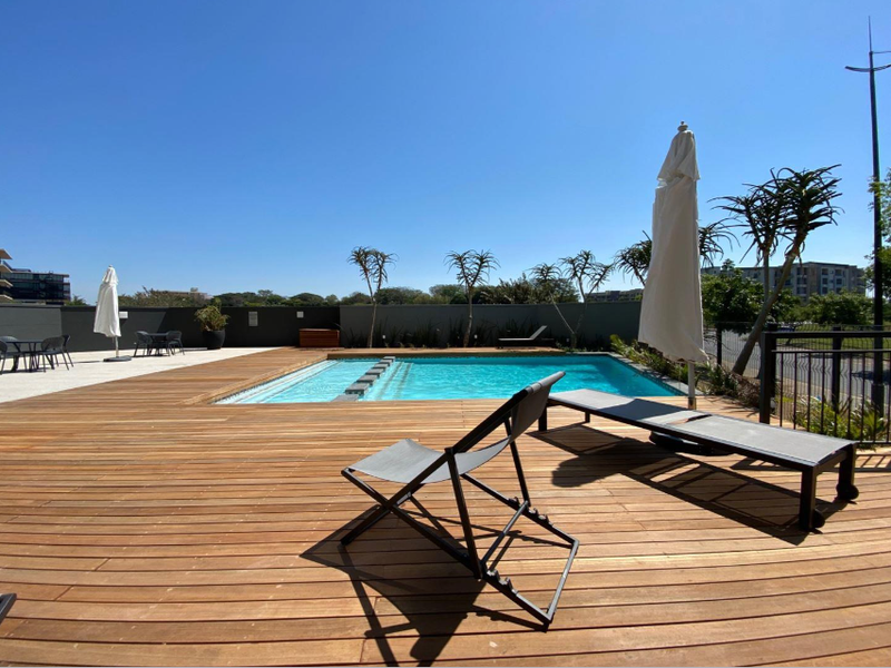 A well-maintained outdoor pool area featuring extensive timber decking, a swimming pool with integrated steps, and secure perimeter boundary walls.