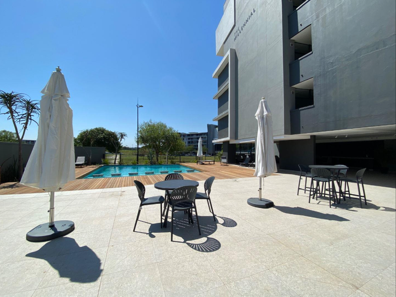 Outdoor pool area featuring a swimming pool, timber decking, and a paved patio space adjacent to a modern apartment building.