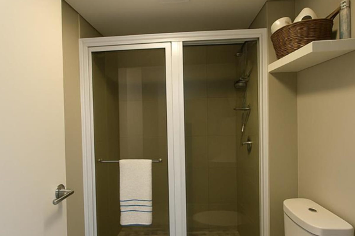 A compact bathroom featuring a glass-enclosed shower, a standard toilet, and a wall-mounted storage shelf.