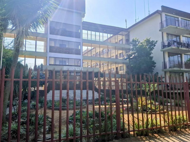 Front view of the Garden View apartment complex featuring a multi-story facade with balconies and a landscaped garden area behind security fencing.