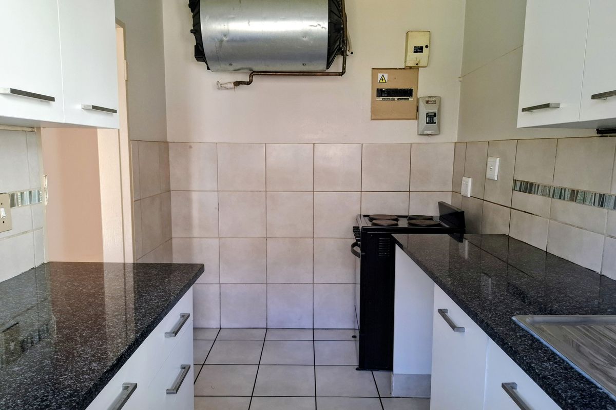 A compact kitchen featuring granite countertops, white cabinetry, tiled backsplash, and an electric stove, with an exposed geyser and electrical board.