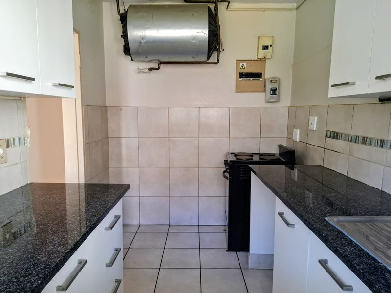 A compact kitchen featuring granite countertops, white cabinetry, tiled backsplash, and an electric stove, with an exposed geyser and electrical board.