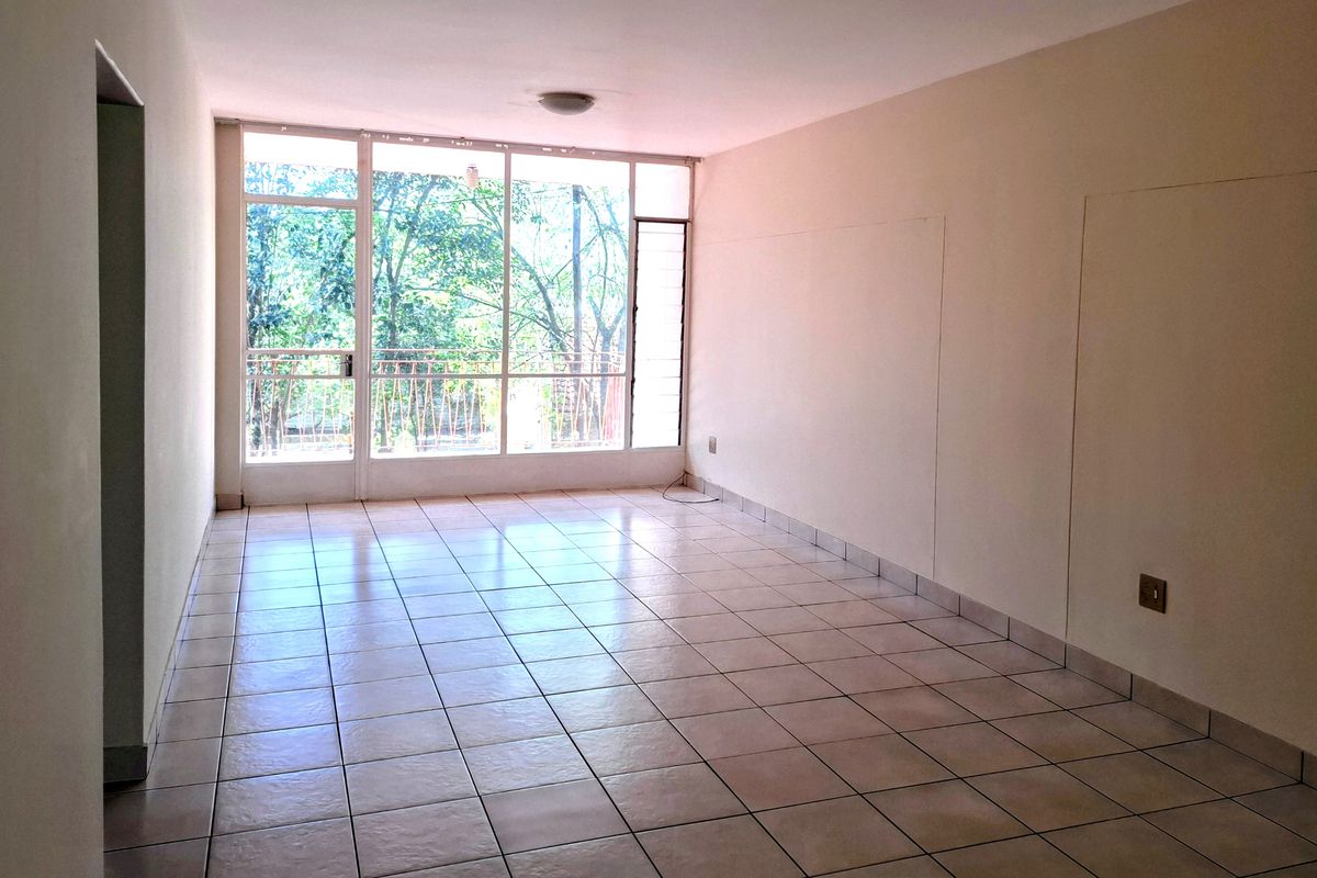 A bright, empty living area featuring ceramic tiled flooring and a large glass window wall providing natural light and access to the balcony.