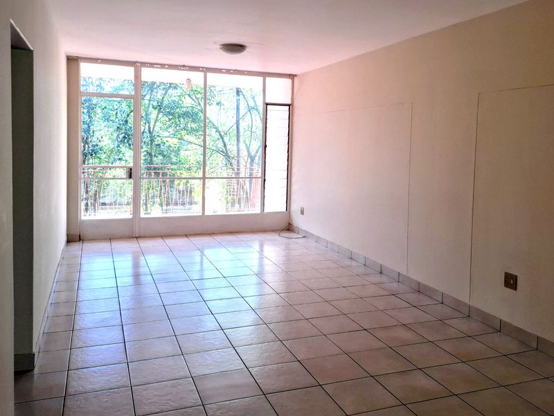 A bright, empty living area featuring ceramic tiled flooring and a large glass window wall providing natural light and access to the balcony.
