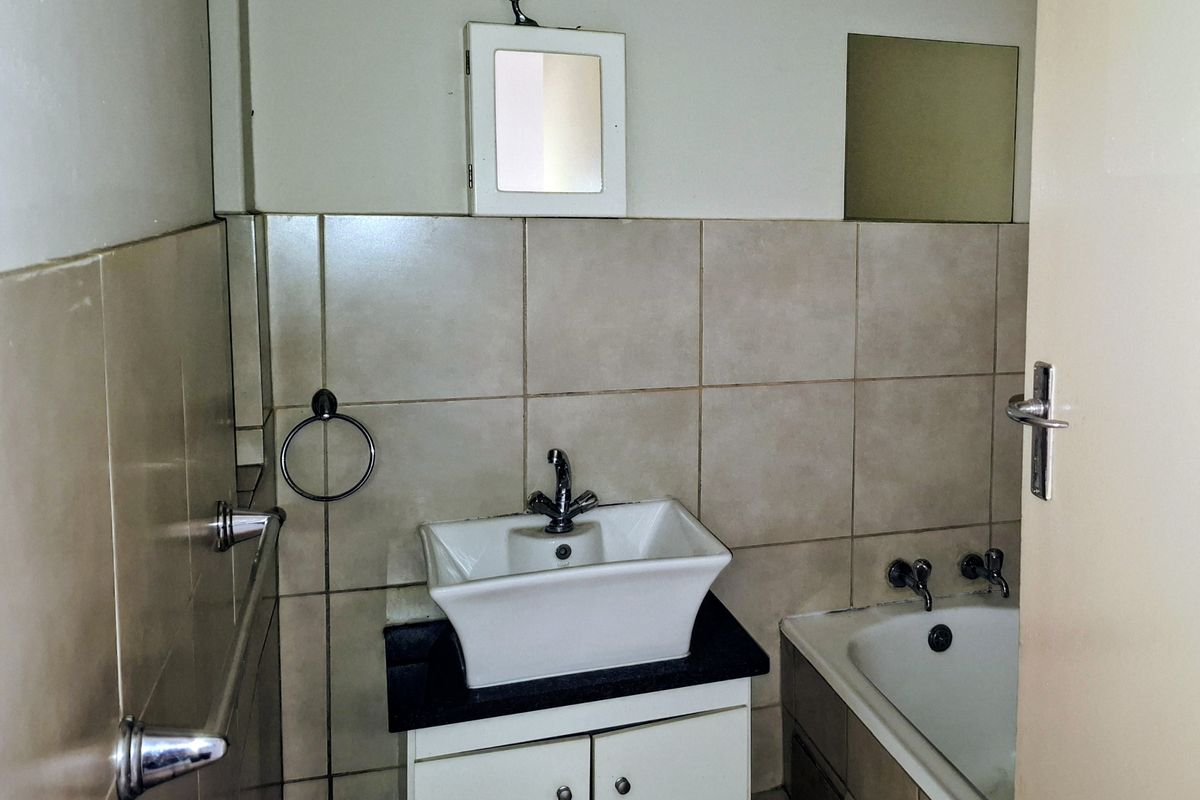A compact bathroom featuring a vessel sink on a vanity cabinet, a bathtub, and neutral wall tiling.