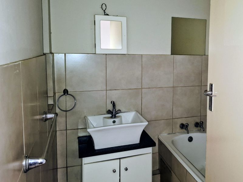 A compact bathroom featuring a vessel sink on a vanity cabinet, a bathtub, and neutral wall tiling.