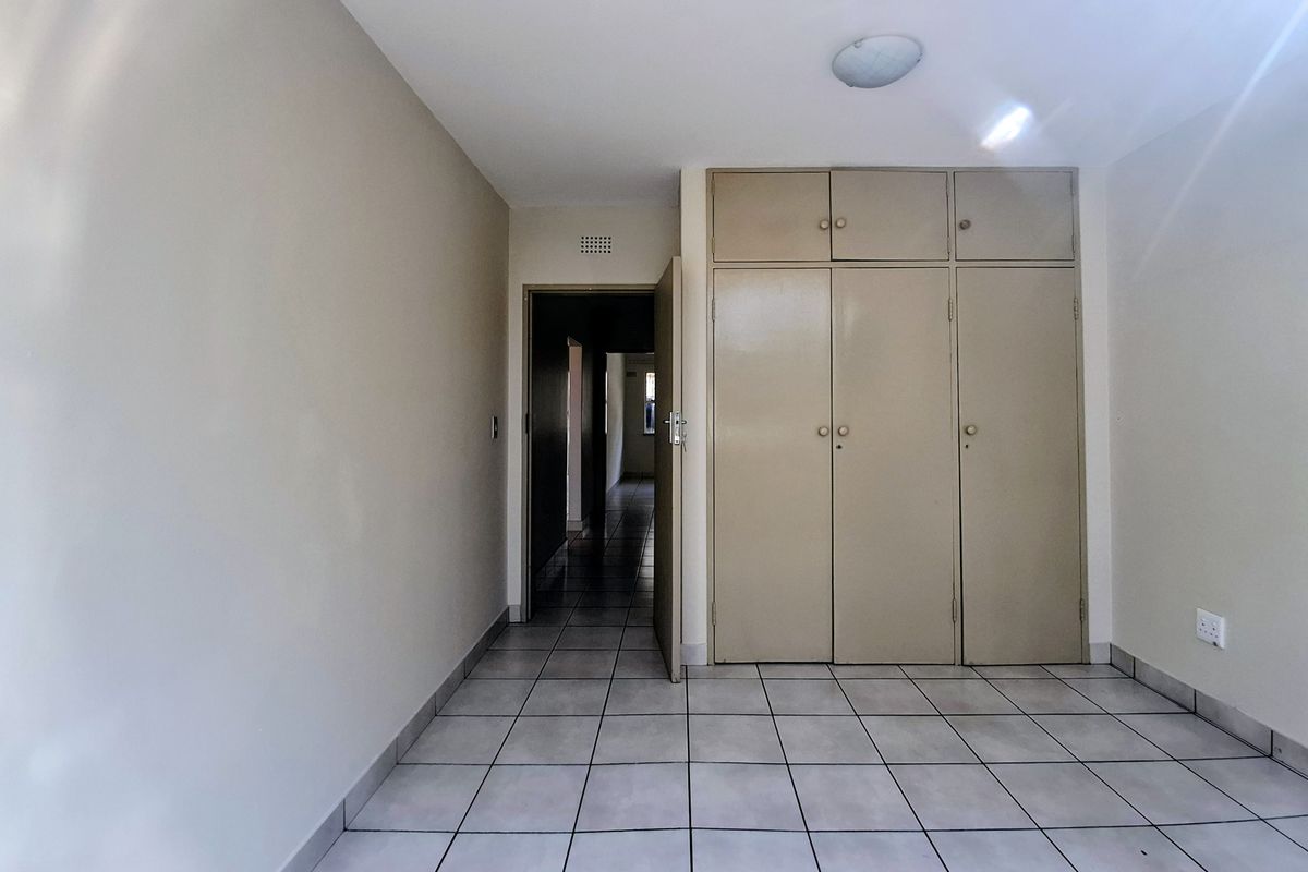 An empty bedroom featuring neutral tiled flooring and built-in storage cupboards, offering a clean and functional space ready for personalization.
