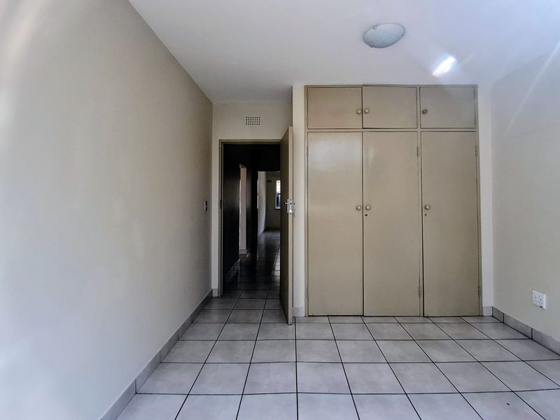 An empty bedroom featuring neutral tiled flooring and built-in storage cupboards, offering a clean and functional space ready for personalization.