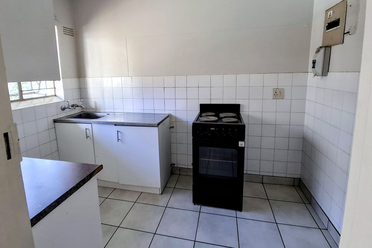 A functional kitchen featuring tiled splashbacks, a stainless steel sink, and basic cabinetry, offering a blank canvas for potential renovation and modernization.