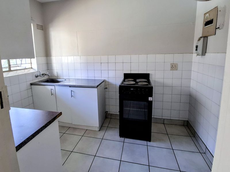 A functional kitchen featuring tiled splashbacks, a stainless steel sink, and basic cabinetry, offering a blank canvas for potential renovation and modernization.