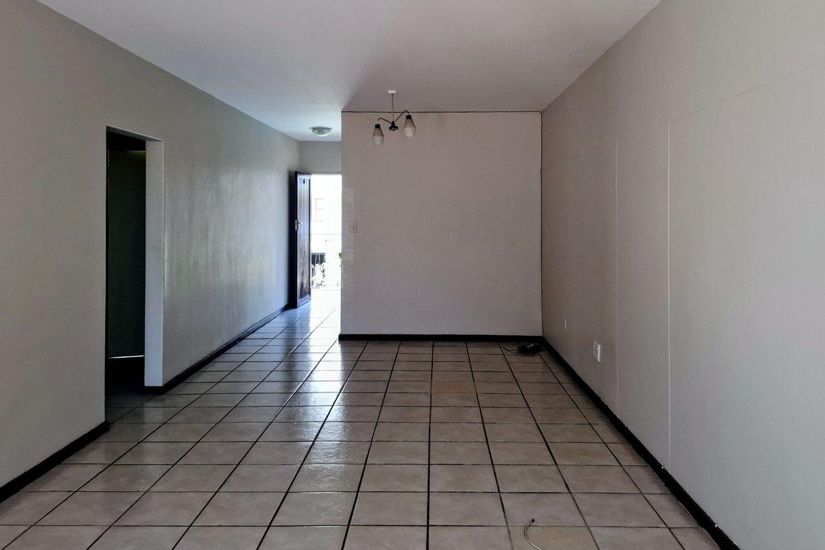 An empty, open-plan living area featuring neutral wall tones and ceramic tile flooring, providing a blank canvas for interior design.