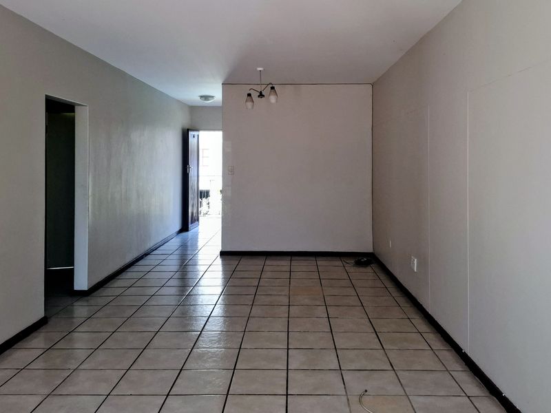 An empty, open-plan living area featuring neutral wall tones and ceramic tile flooring, providing a blank canvas for interior design.