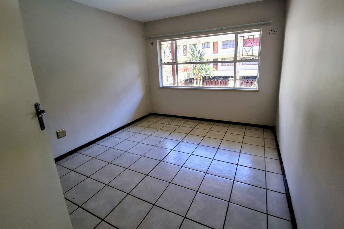 A bright, empty bedroom featuring neutral walls, tiled flooring, and a large window with security bars, offering a clean canvas for personalization.