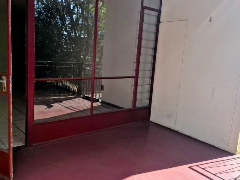An outdoor balcony area featuring a painted concrete floor and a large metal-framed glass partition leading into the apartment interior.