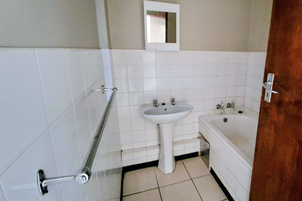 A dated bathroom featuring a white pedestal basin, bathtub, and tiled finishes, presenting an opportunity for modernization and renovation.