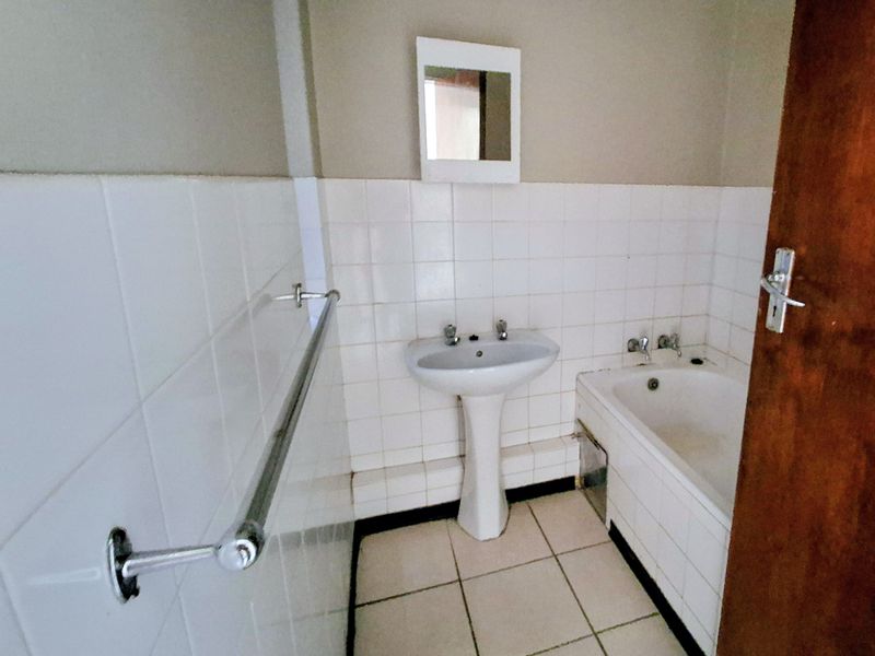 A dated bathroom featuring a white pedestal basin, bathtub, and tiled finishes, presenting an opportunity for modernization and renovation.
