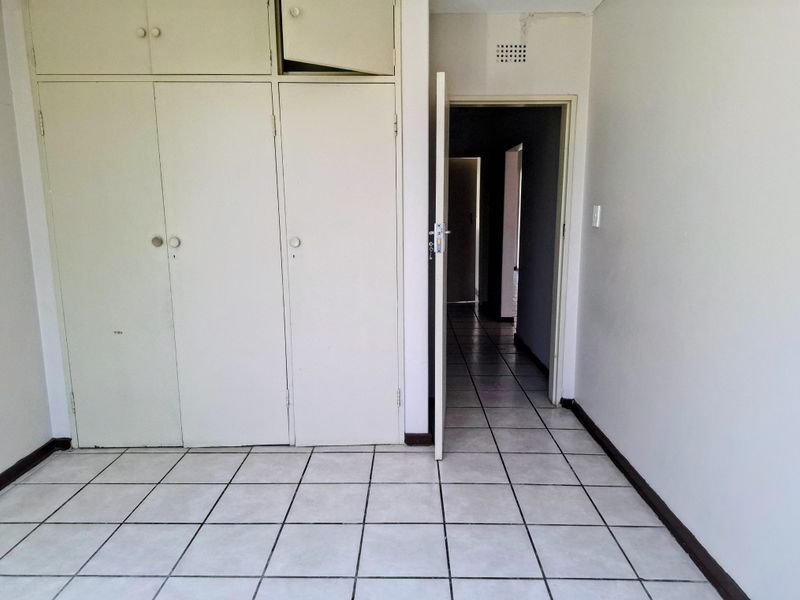 An empty bedroom featuring built-in cupboards, ceramic tiled flooring, and direct access to a hallway.