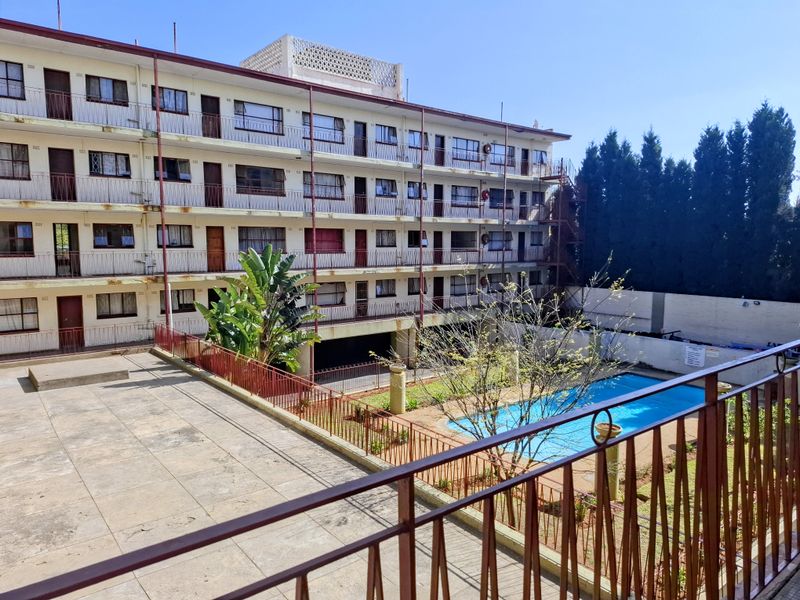 Rear view of a multi-story apartment complex featuring a communal swimming pool, paved courtyard area, and metal balcony railings.